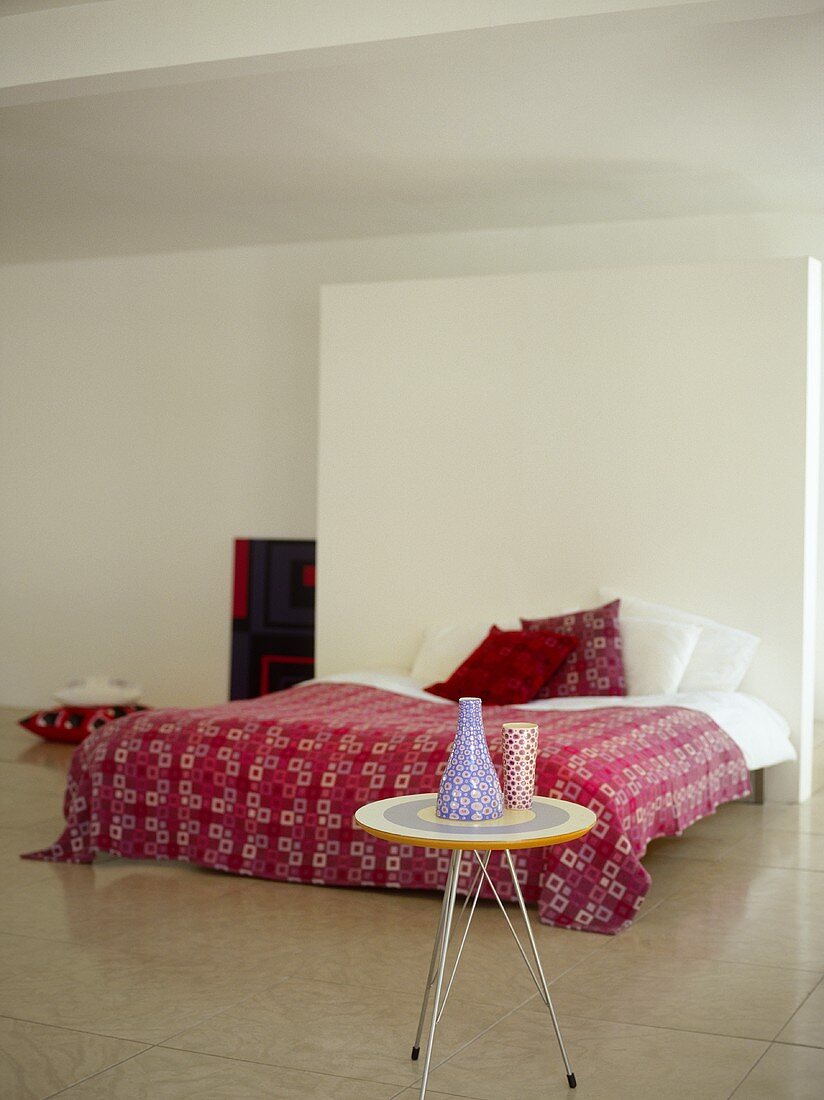 Beistelltisch in Retro-Stil vor Doppelbett mit gemusterter Tagesdecke