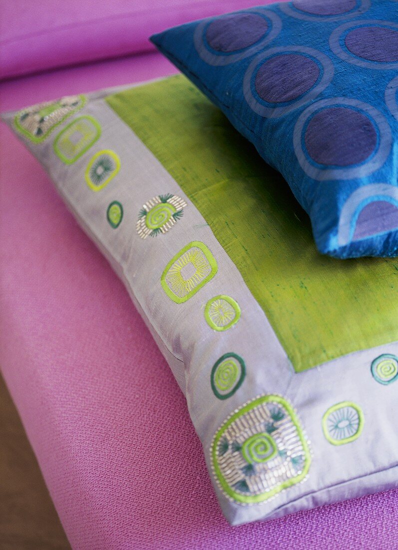A detail of embroidered and pattern cushions on a pink sofa,