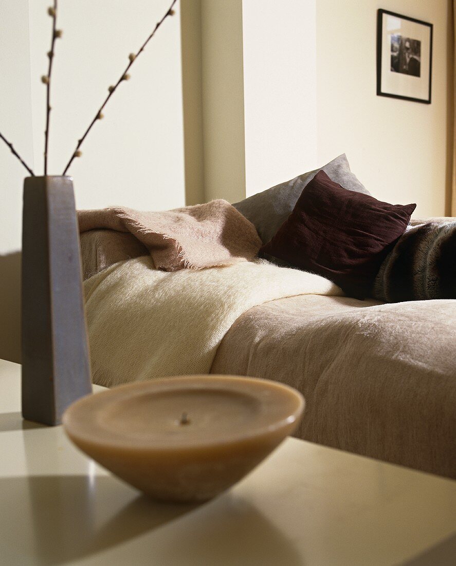 Vase and candle on a table in front of a couch with cushions
