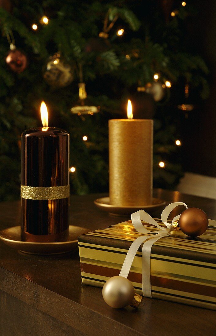 Brennende Kerzen mit glänzender und matter goldener Oberfläche neben Geschenkpaket
