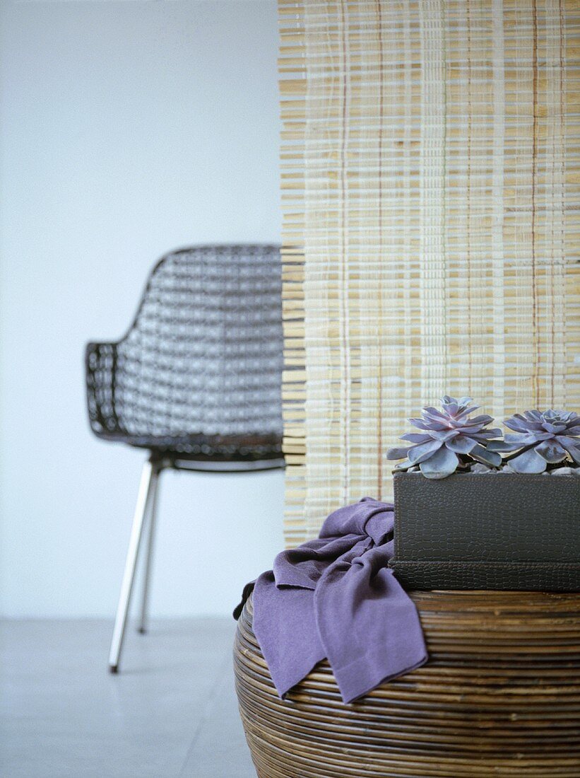 A detail of a wooden round table, a neutral blind and an open weave style chair in the background