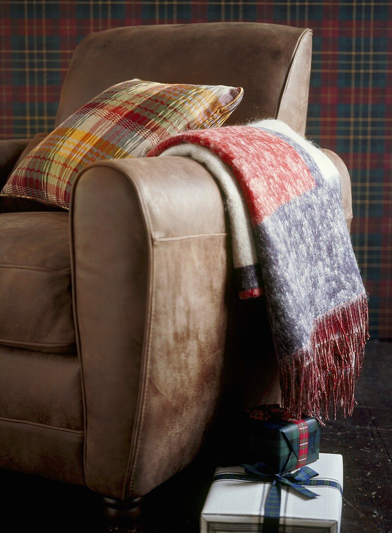 A detail of a tan leather armchair with woollen throw and cushion,