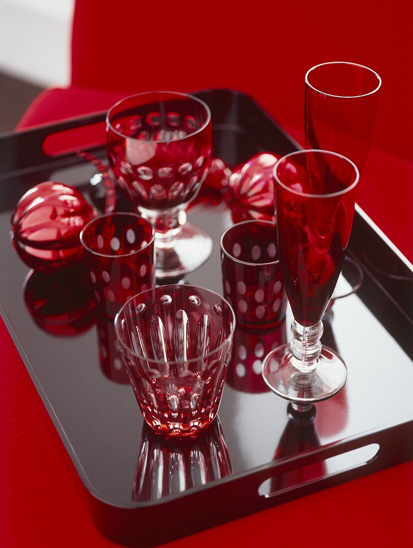 Rote Gläser auf schwarzem glänzenden Tablett und rotem Untergrund