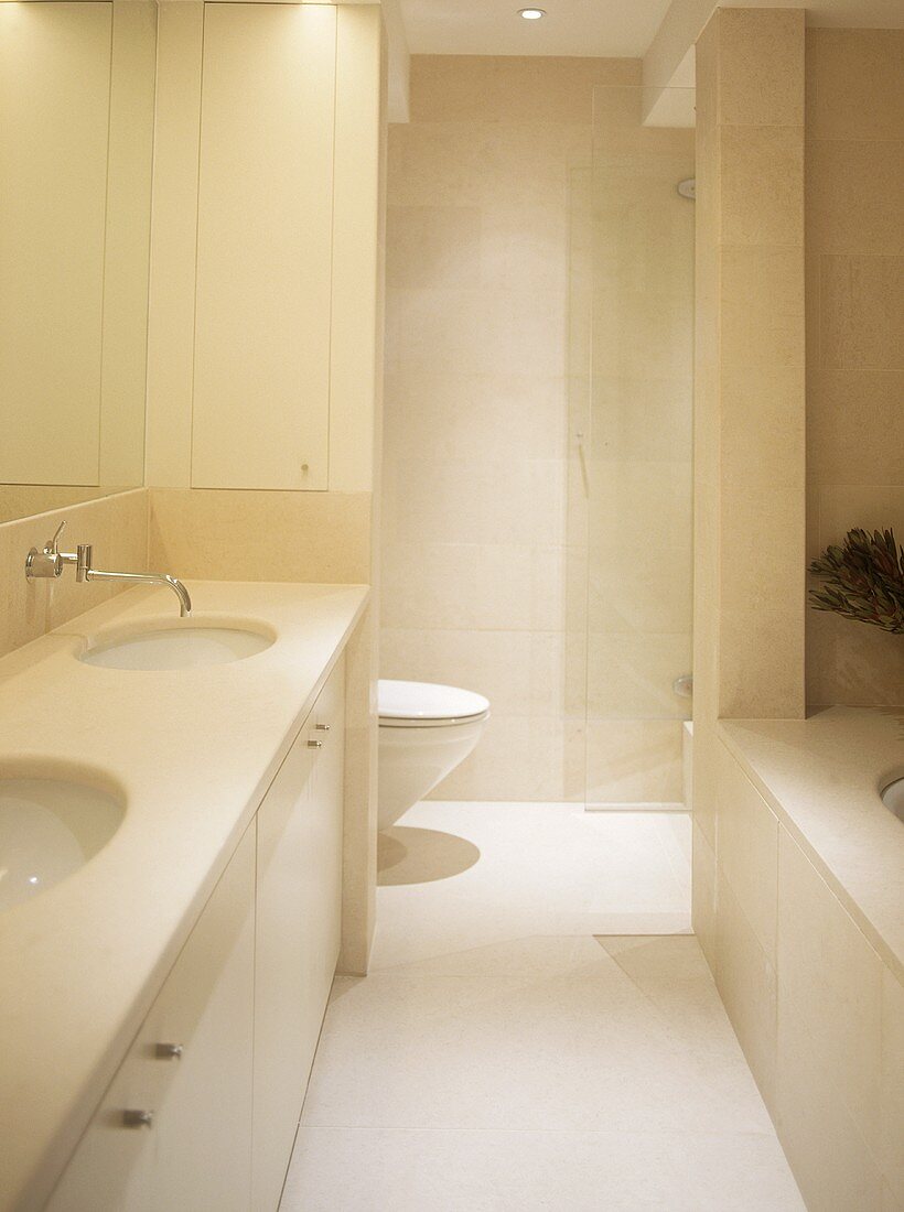 Cream bathroom with two built in washbasins, bath tub and toilet behind partition.