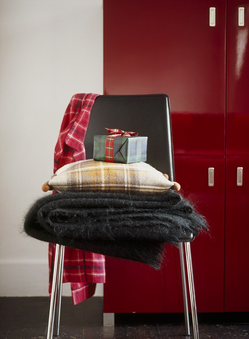 Schwarzer Stuhl mit Wolldecke, Kissen und Geschenkpaket vor rotem Schrank