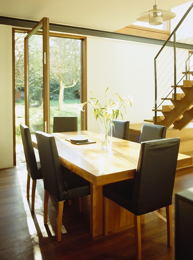 Wooden dining table with black leather dining chairs in open plan room with patio door