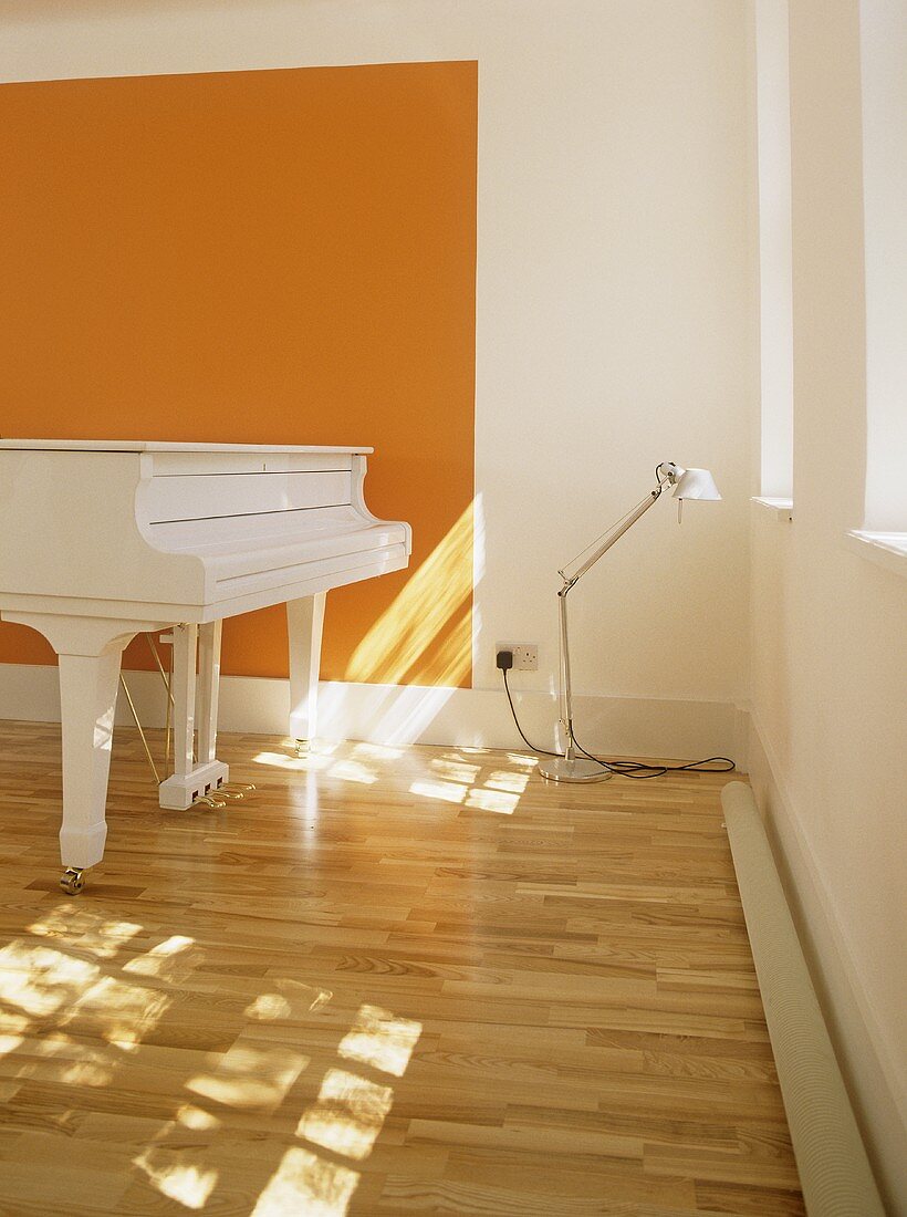 A modern, white and orange minimalist music room, grand piano, wooden floor, lamp,