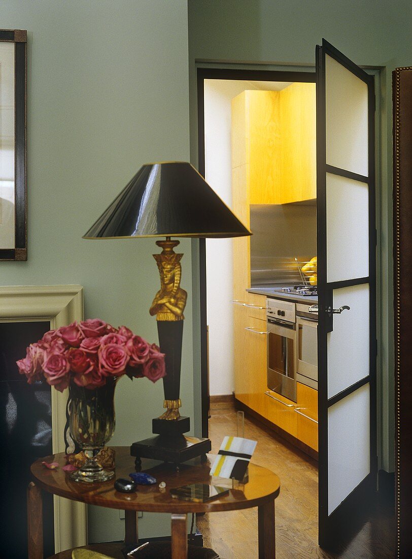 Wohnzimmer mit Beistelltisch und antiker Tischlampe vor offener Tür mit Blick in gelbe Designerküche