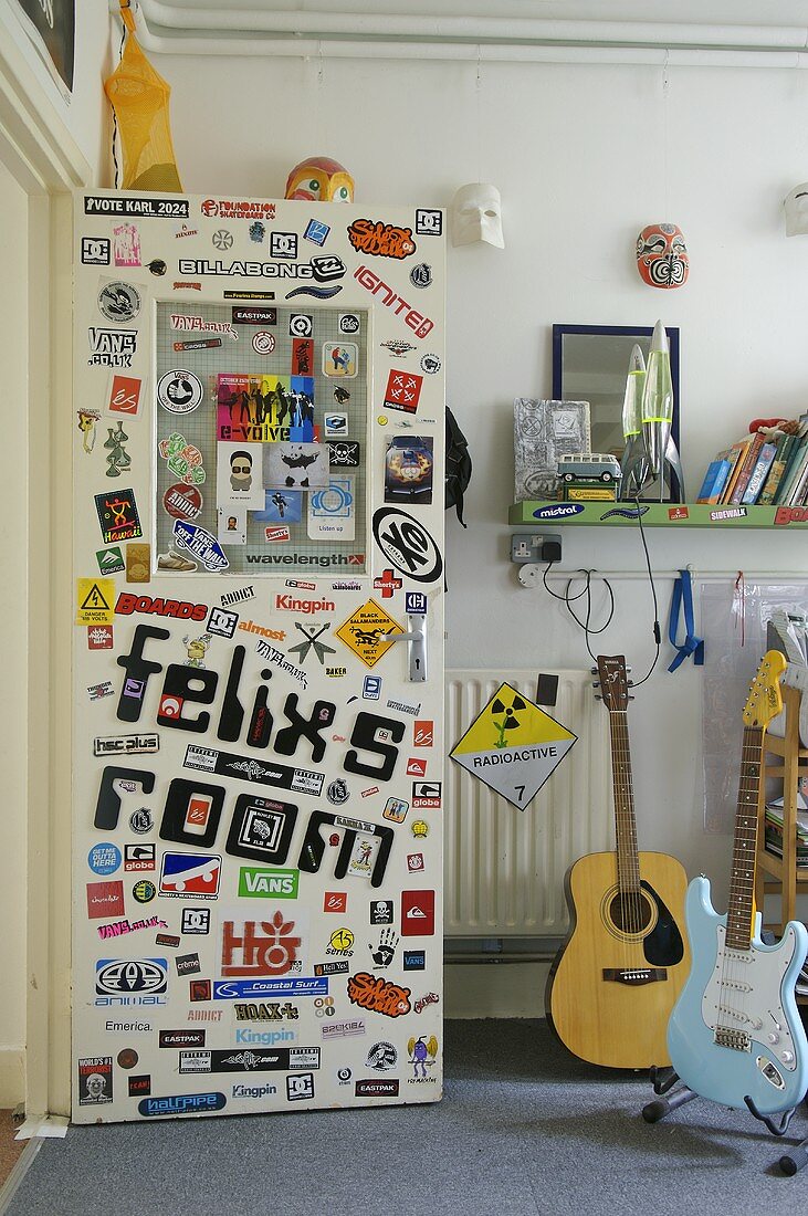 Door of teenagers room covered with various stickers next to guitar on stand