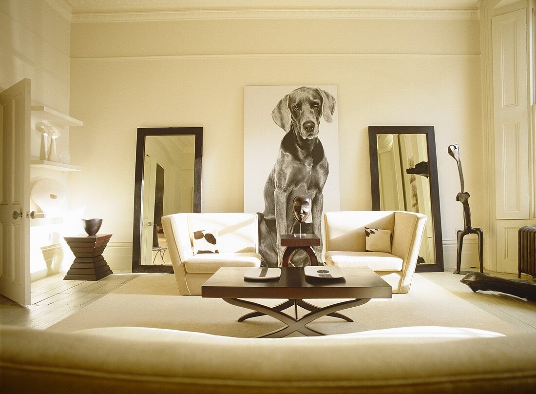 Wohnzimmer mit weisser Sofagarnitur und Standspiegeln neben großem Bild mit Hundemotiv