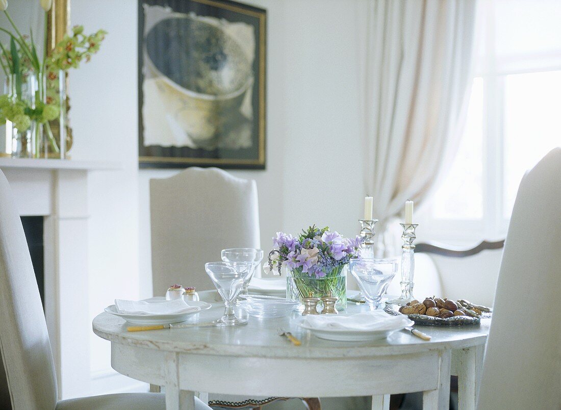 A detail of a traditional, neutral dining room with painted wooden table and upholstered chairs