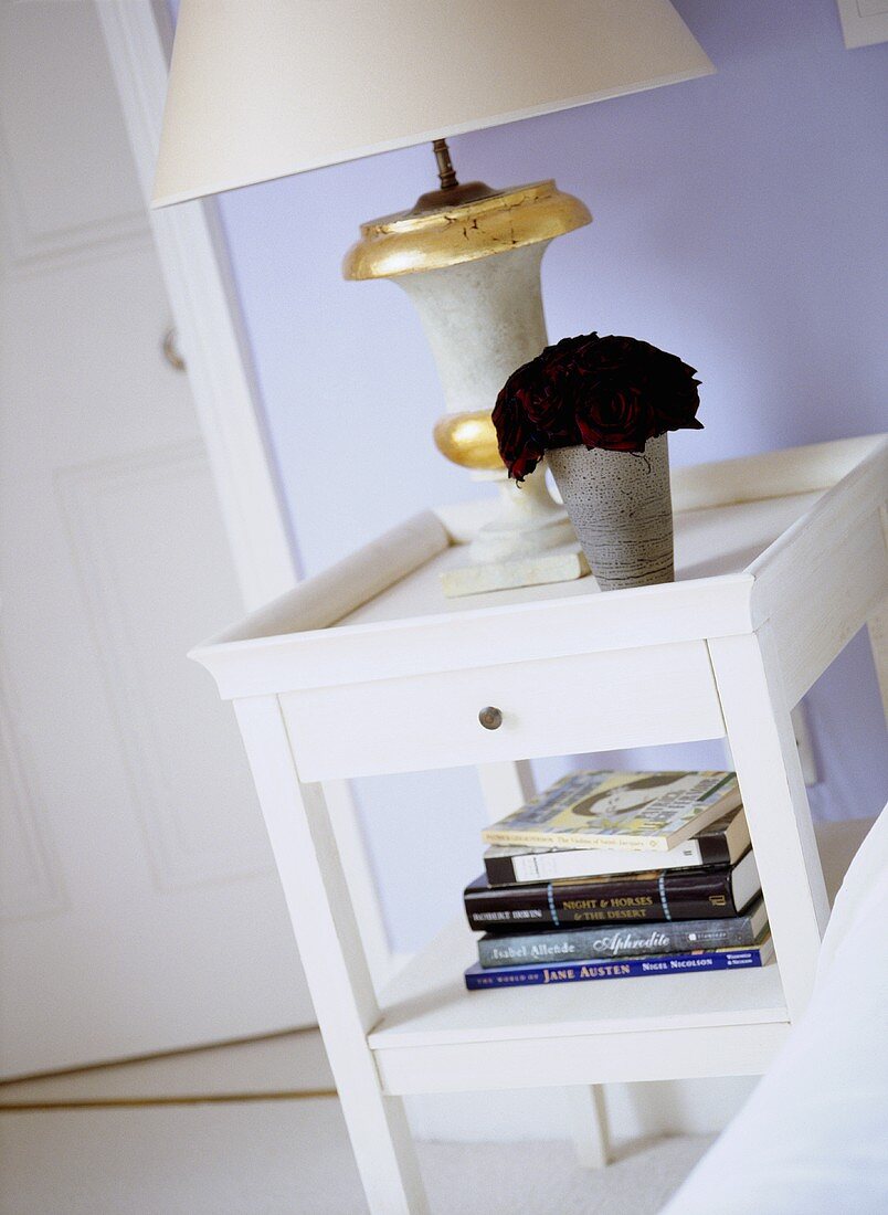 A detail of a pale blue bedroom, showing a white painted bedside table, lamp and books