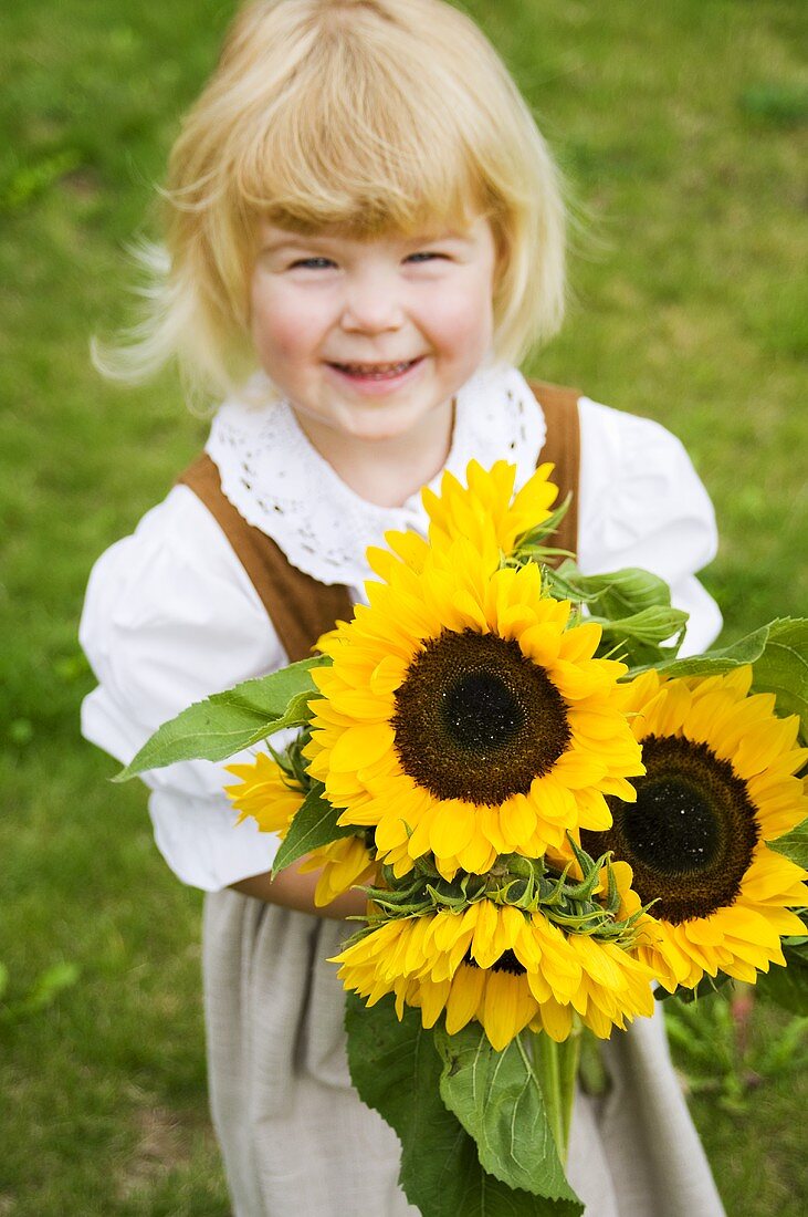 Mädchen in Trachtenkleid hält Blumenstrauss mit Sonnenblumen