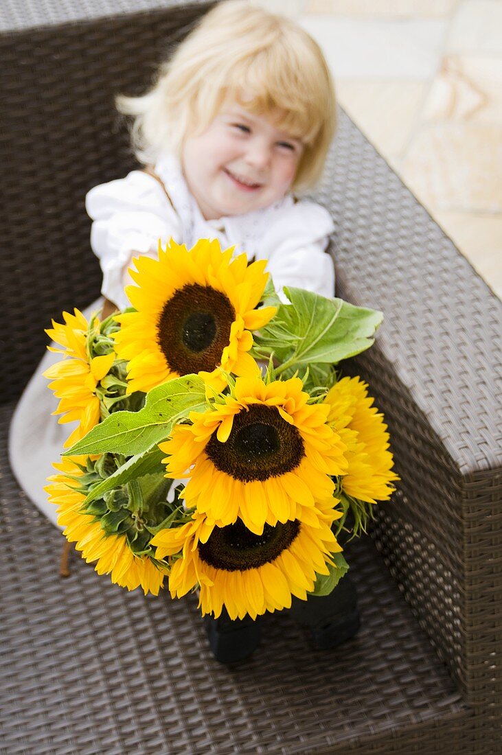 Little girl sitting in a chair holding a bouquet of sunflowers