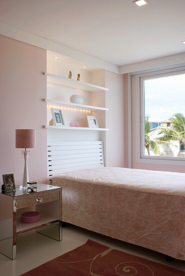 Ein Einbettzimmer mit Regalen über dem Bett in der Wandnische und ein Nachttisch