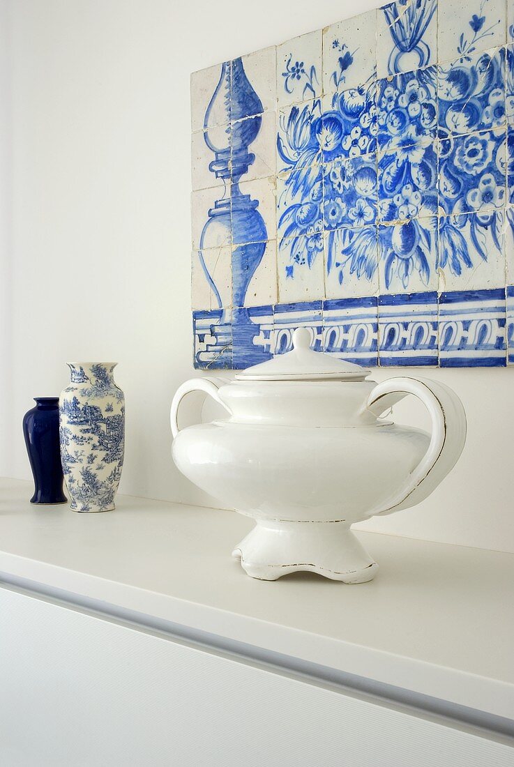 Ein Azulejo aus blau-weissen Keramikfliesen über einer Ablage mit einem Suppentopf und Vasen