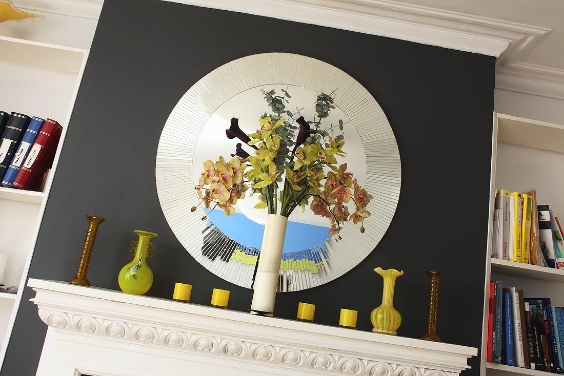 A vase on a white mantelpiece and a round mirror set into the black chimney breast