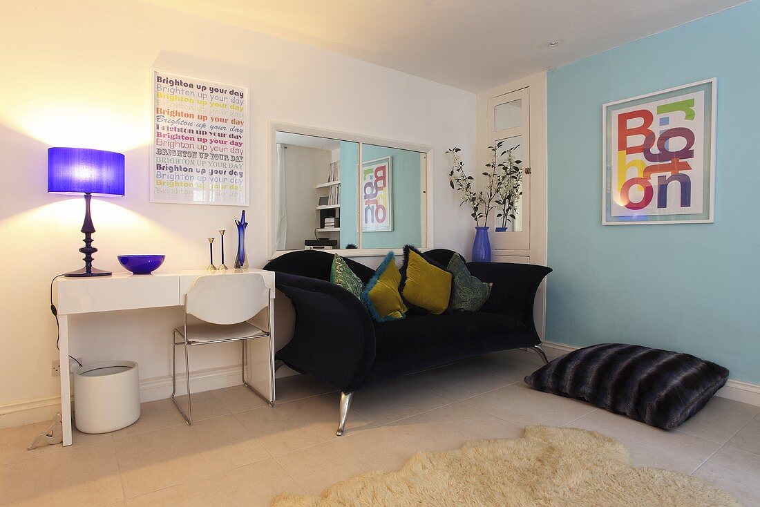 Ein dunkelblaues Sofa mit Dekokissen, ein Bodenkissen und ein weisser Schreibtisch in einem Wohnzimmer