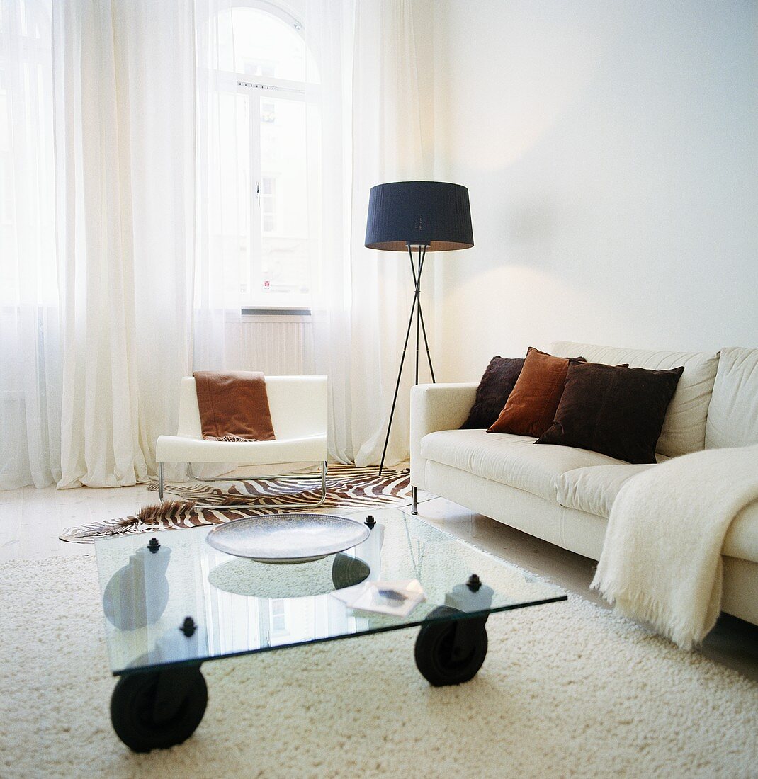 Eine Stehlampe neben einem weisen Sofa und ein Couchtisch aus Glas im Wohnzimmer