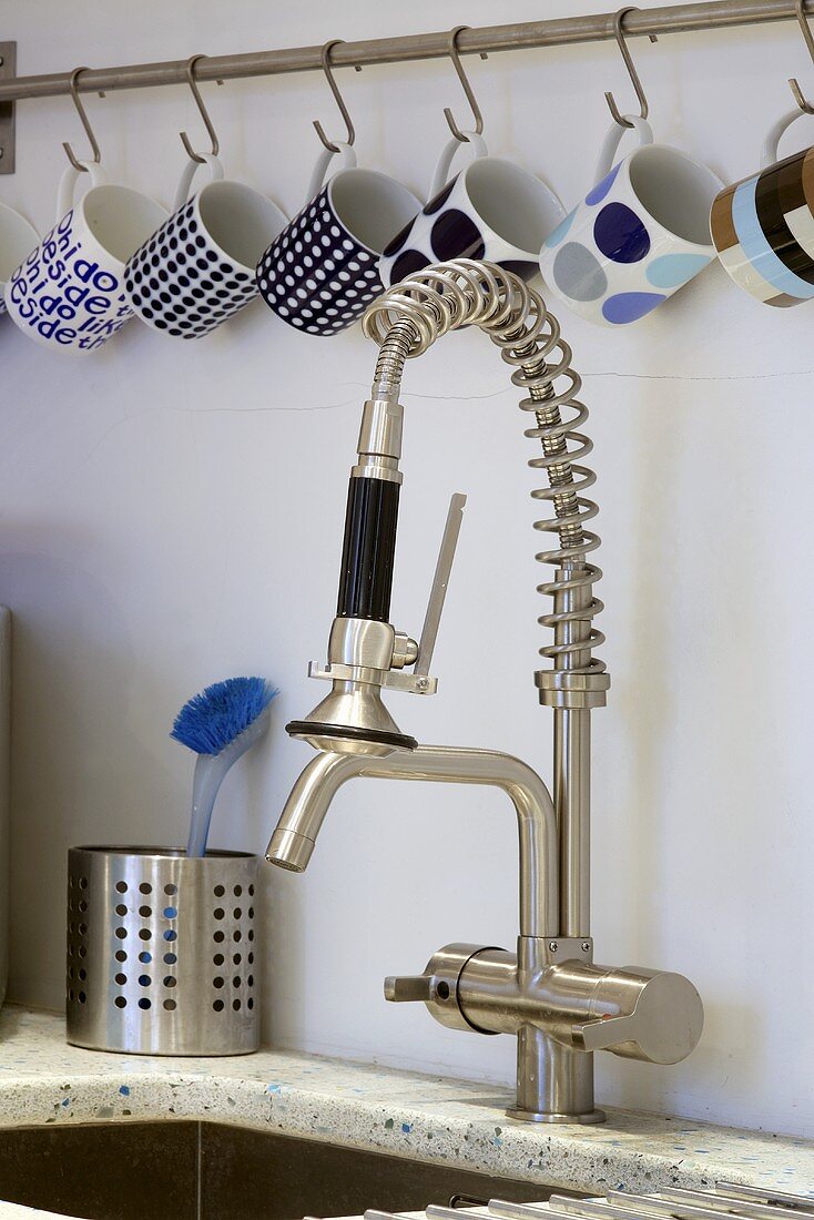 Cups hanging from hooks above a kitchen tap