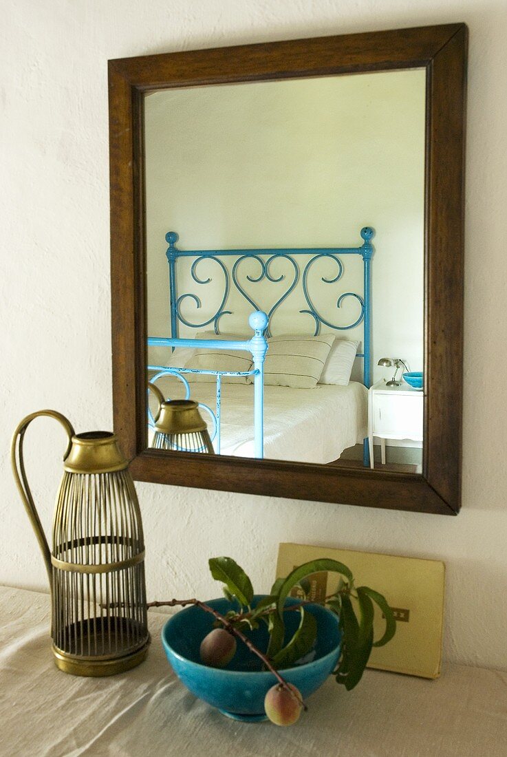 Fruit in a blue bowl and an antique bottle holder in front of a mirror reflecting a blue wrought iron bed