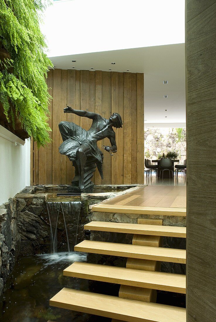 Kleiner Wasserfall mit einer Skulptur neben einer schwebenden Treppe am Eingang