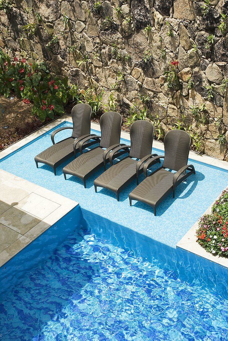 A pool with loungers in front of a natural stone wall
