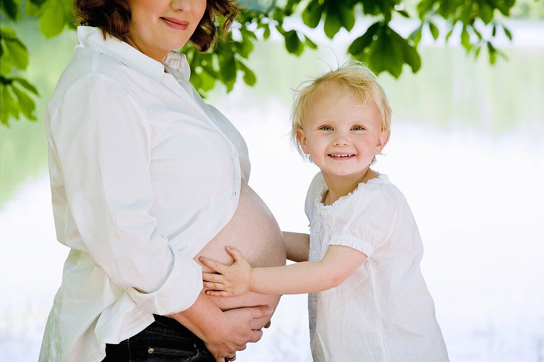 Kleines Mädchen hält den Bauch der schwangeren Mutter