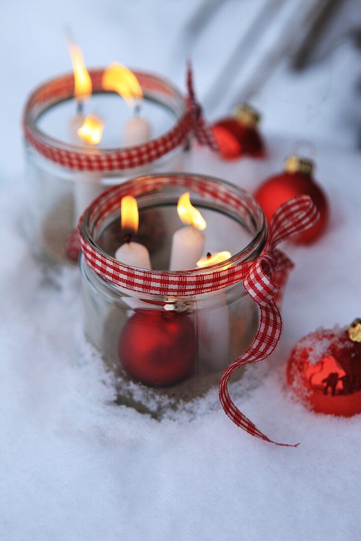 Burning candles in a jar and a Christmas baubles in the snow