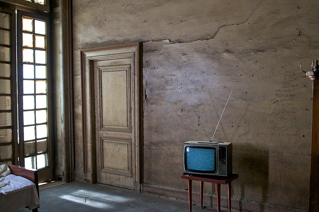 Wohnraum mit altem Fernseher auf Tischchen vor brauner Wand mit Holztür