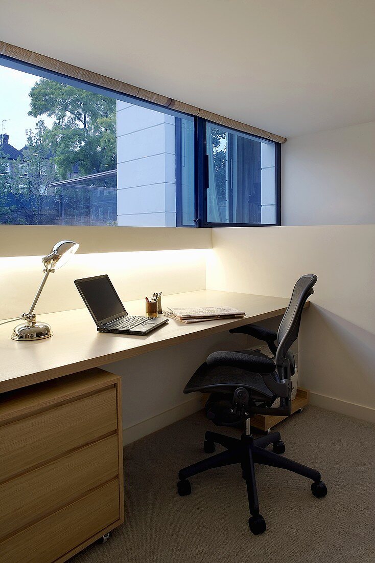 Modernes home office unter Fensterband mit Retro-Tischlampe neben Notebook