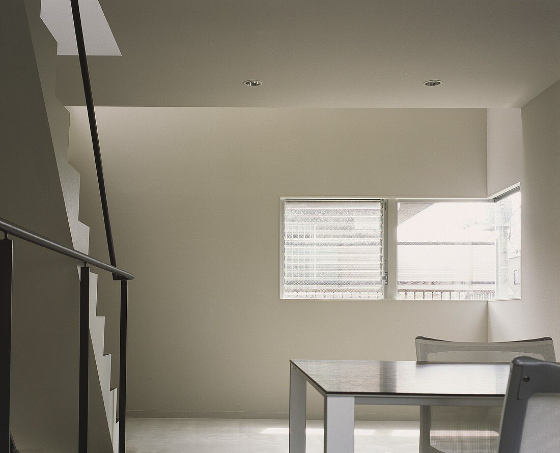 Minimalistischer Wohnraum mit Treppenaufgang und Tisch mit Stuhl vor Fenster