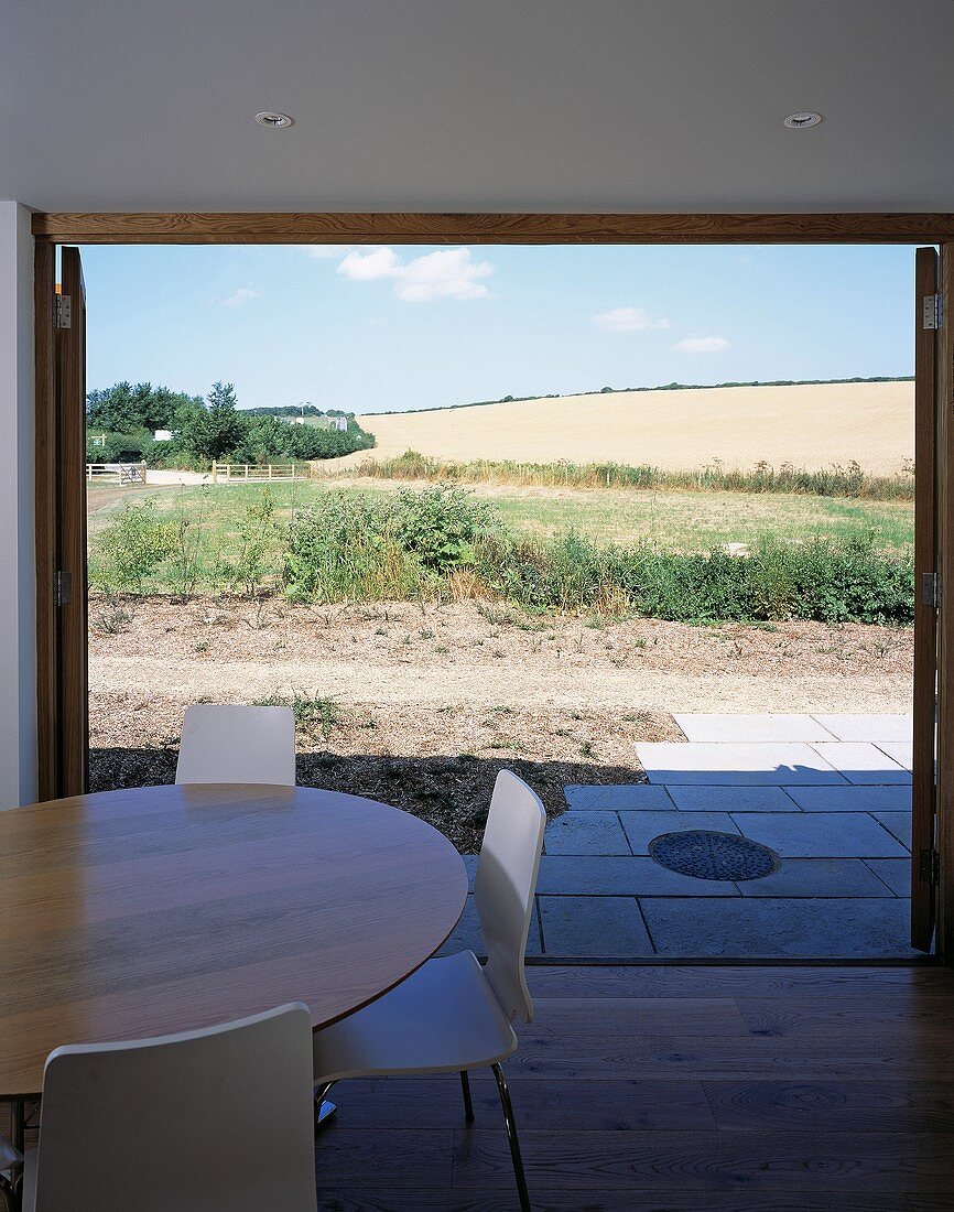 Esstisch mit weissen Stühlen vor offenen Terrassentüren und Blick auf sonnigen Garten
