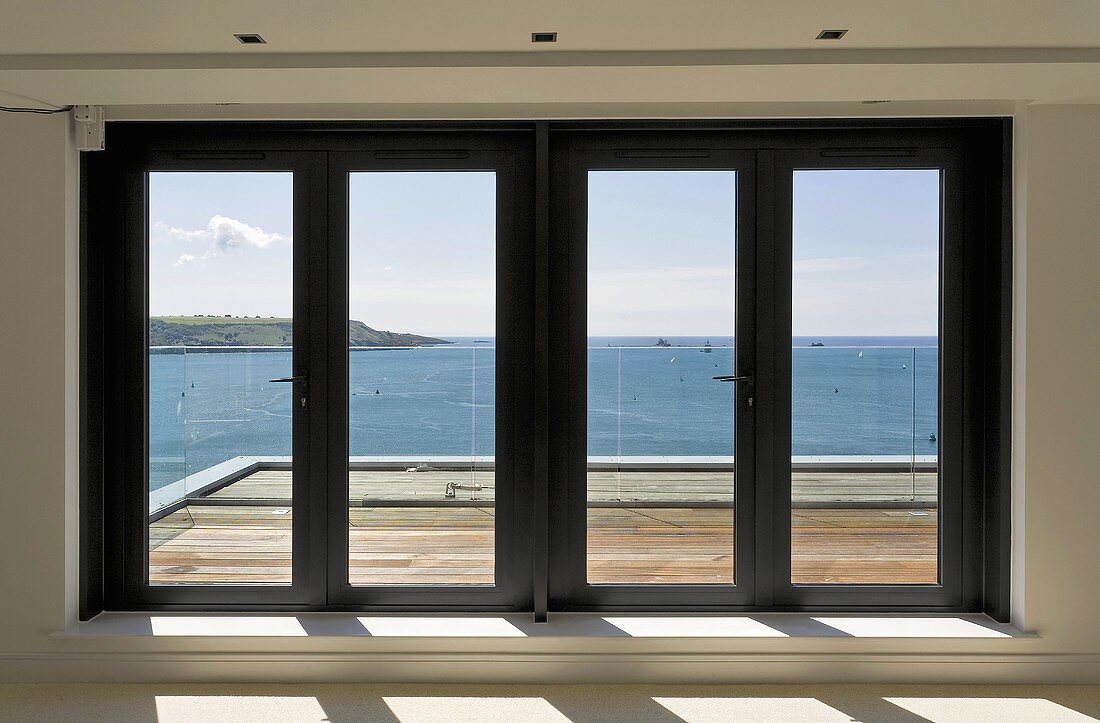 Glass patio doors in front of wood deck with a view of the ocean
