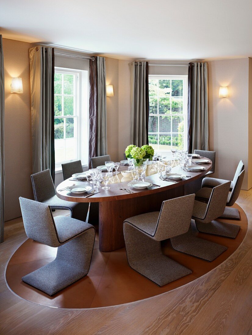 Classic dining room with cantilevered chairs upholstered in gray around an oval table and gray floor length curtains at the window