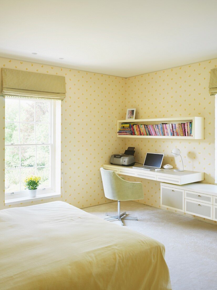 Helles Schlafzimmer mit home office in Ecke und gelbgemusterter Tapete an Wand