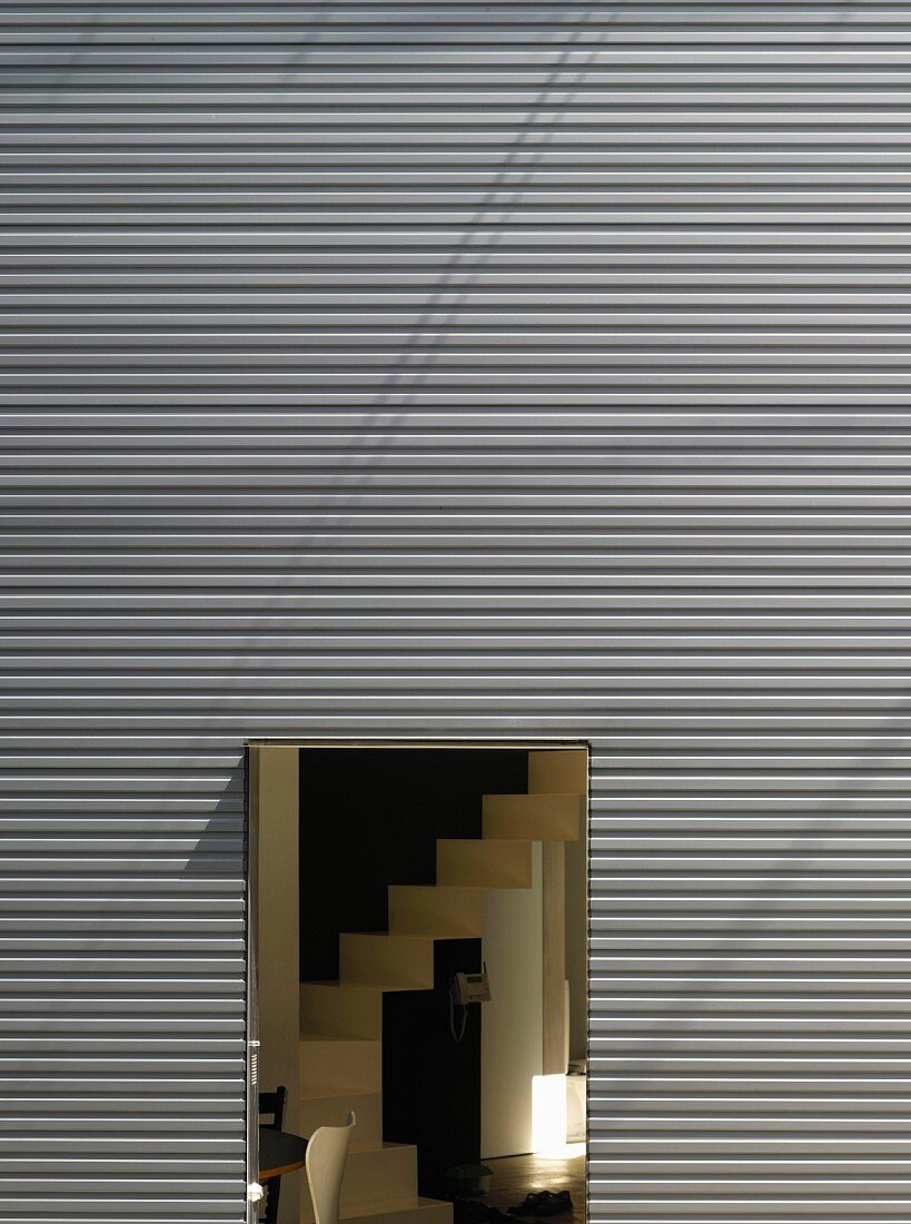 House facade made of trapezoidal sheet metal with an open door and view of a staircase
