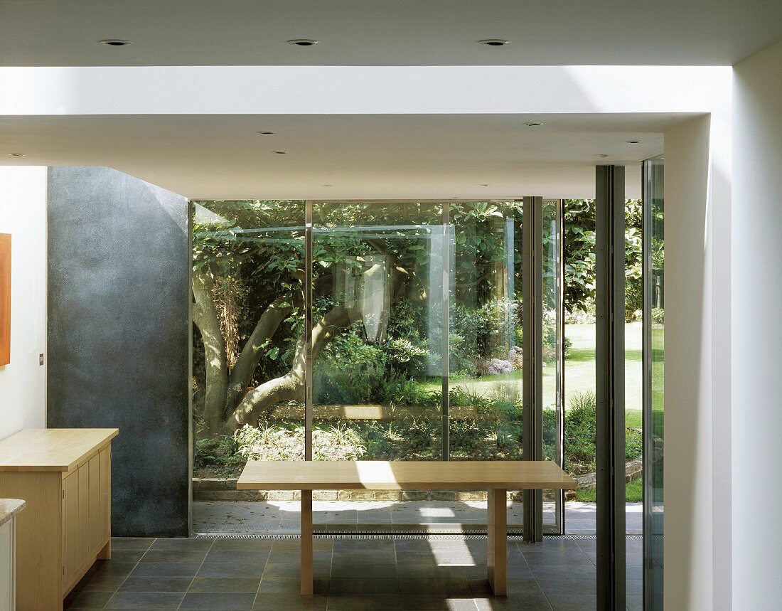 Esstisch und Sideboard aus hellem Holz vor Glasfront mit Gartenblick
