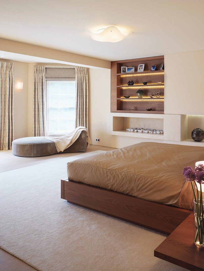 Double bed with light brown bed linen and modern divan in front of built-in shelves in a spacious bedroom