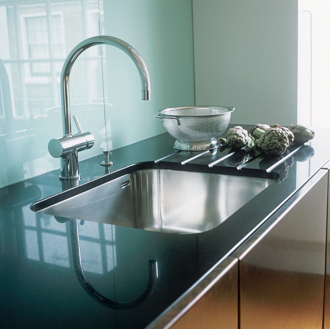 A sink in front of a glass backsplash
