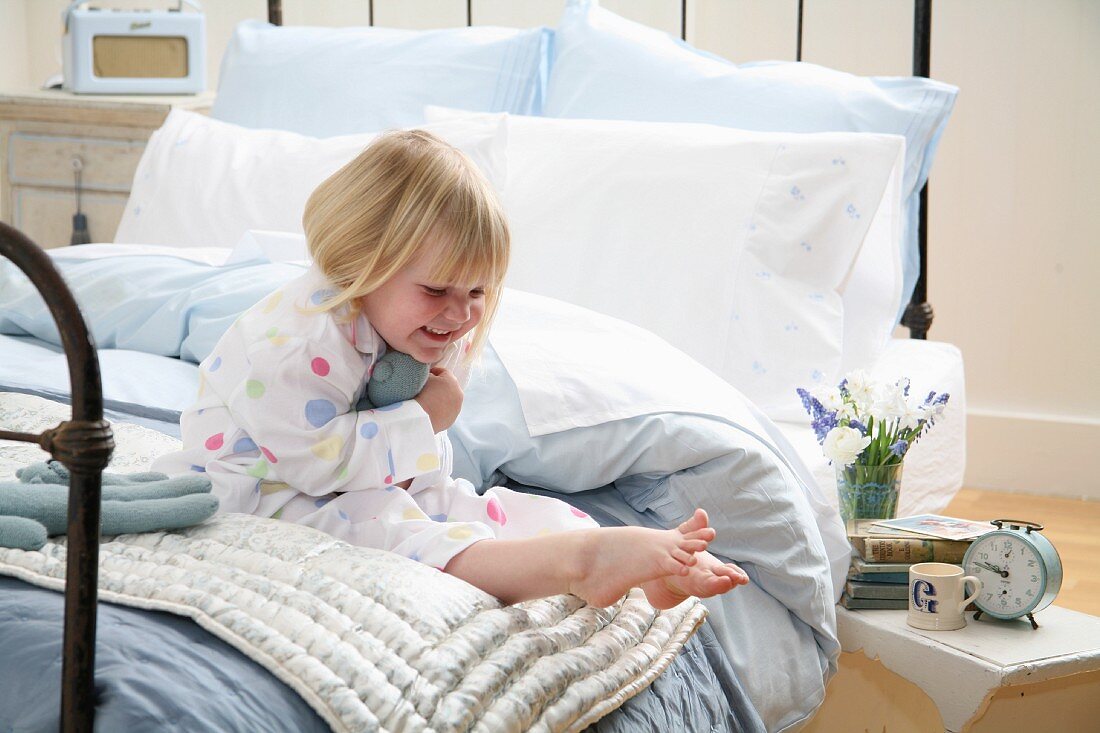 Kleines Mädchen im Schlafanzug sitzt auf dem Bett