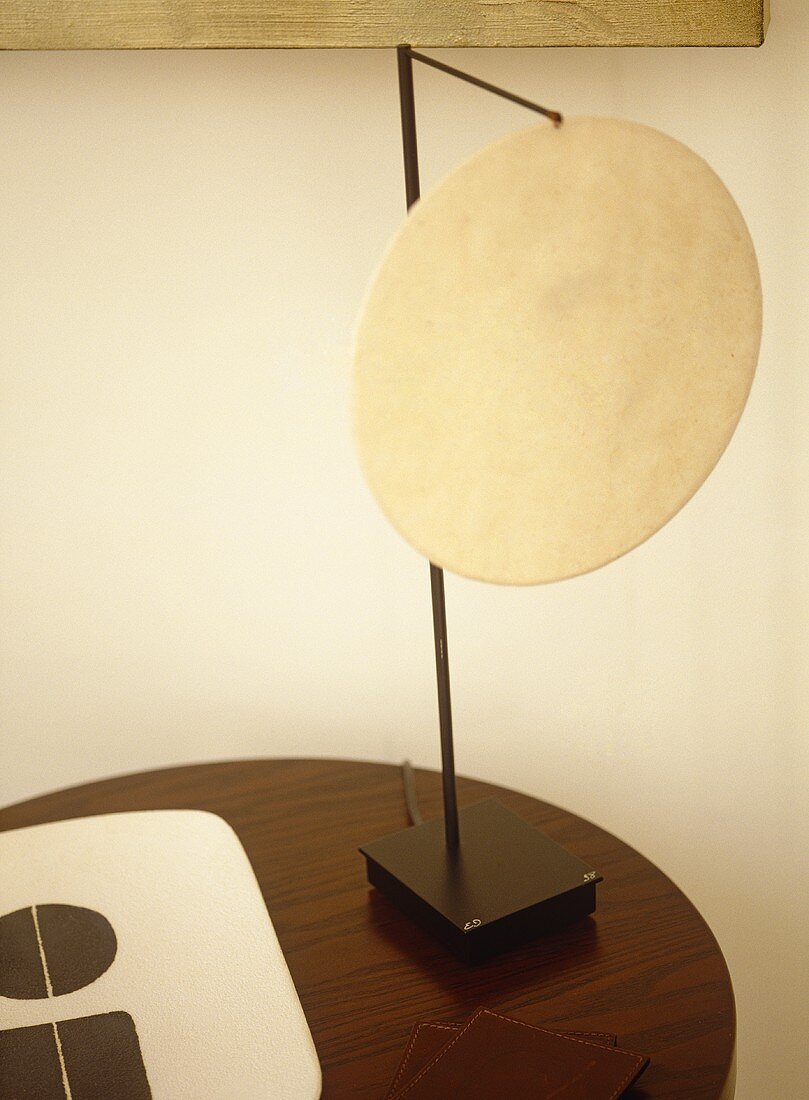 Lamp with circular neutral shade on round wooden table.