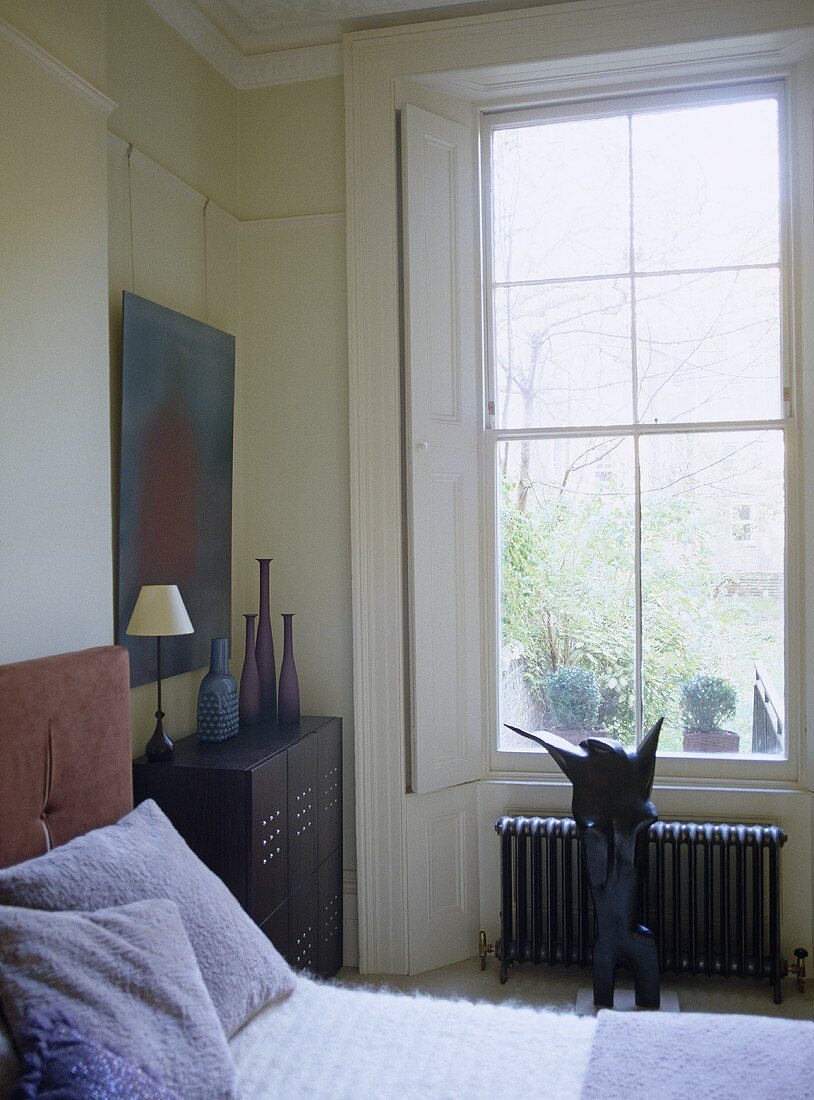 Bedroom with ornaments and sculpture under window with shutters.