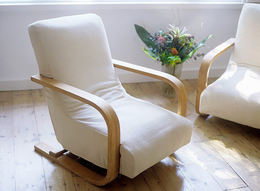 White cotton armchairs with vase of flowers on wooden floor.