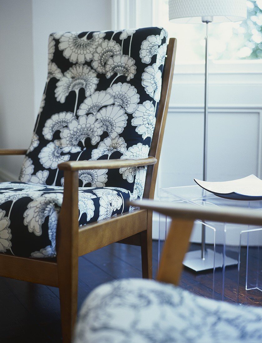 A detail of a modern, sitting room, a retro style upholstered armchair with pattern fabric, side table, lamp,