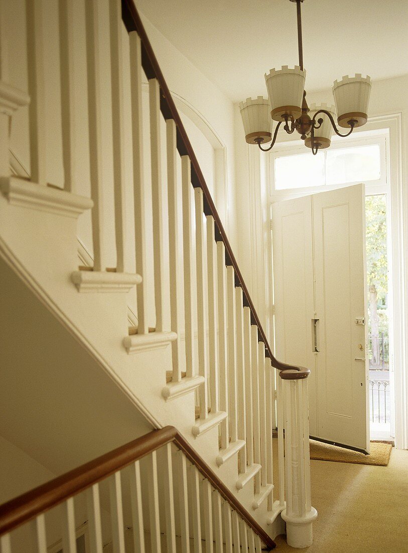 Treppe mit Geländer aus Holz in weißem Flur und offene Haustür