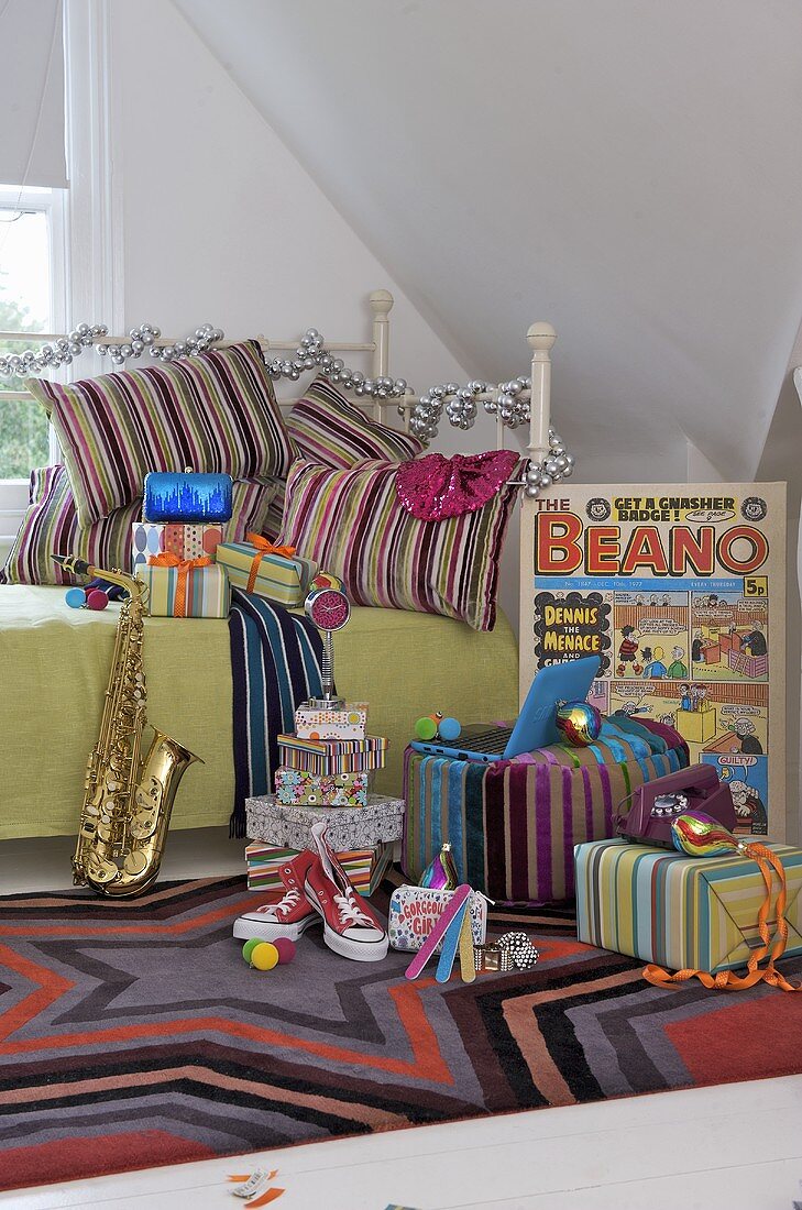A musical instrument and a presents on a bed against a pile of cushions and on the floor