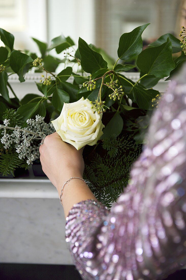 weiße Rose in Hand haltend vor einem Gesteck