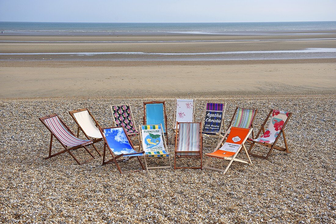 Deckchairs with various patterned fabrics on a beach with a view of the sea