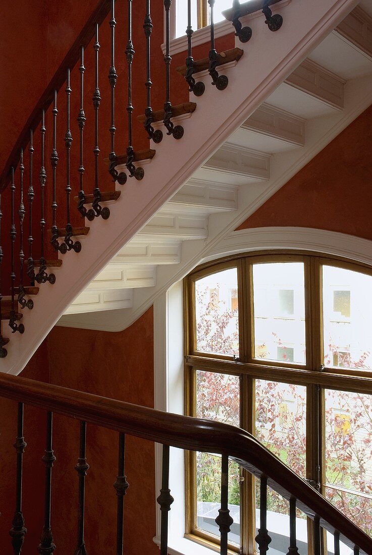 Treppenhaus mit Holzgeländer an Treppe und rotbrauner Wand